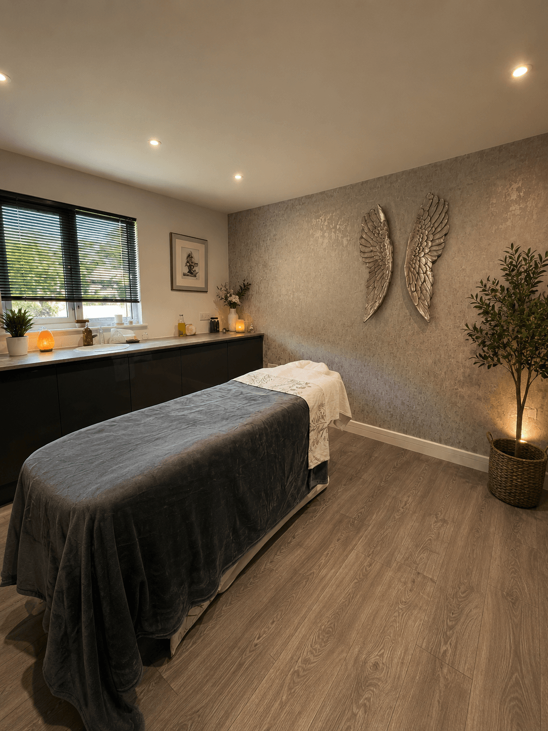 Inside the Nurture Body Therapy treatment room in Ashford, Kent — warm low lighting, draped massage table, salt lamp and silver angel-wing wall art